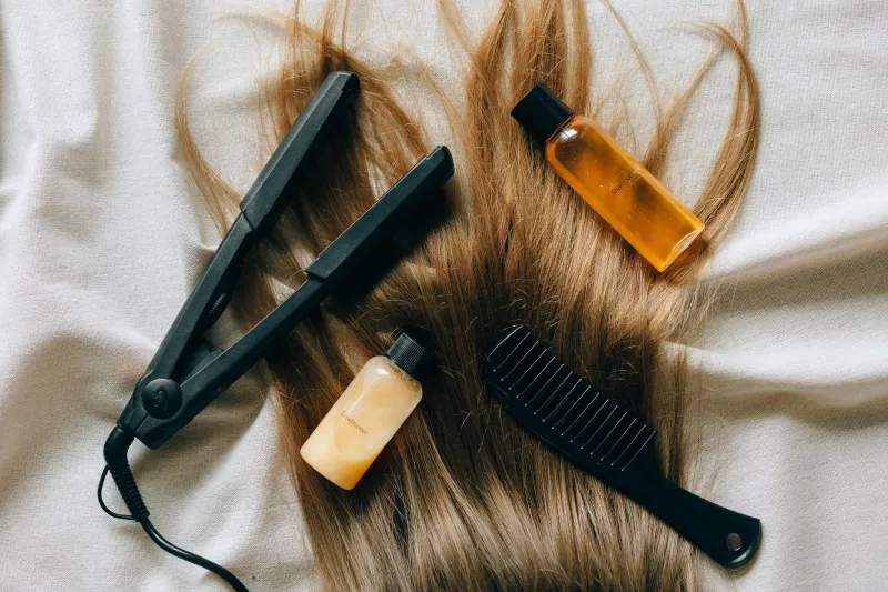 Flat iron, two hair care products, and a comb arranged on brown hair for botox hair treatment