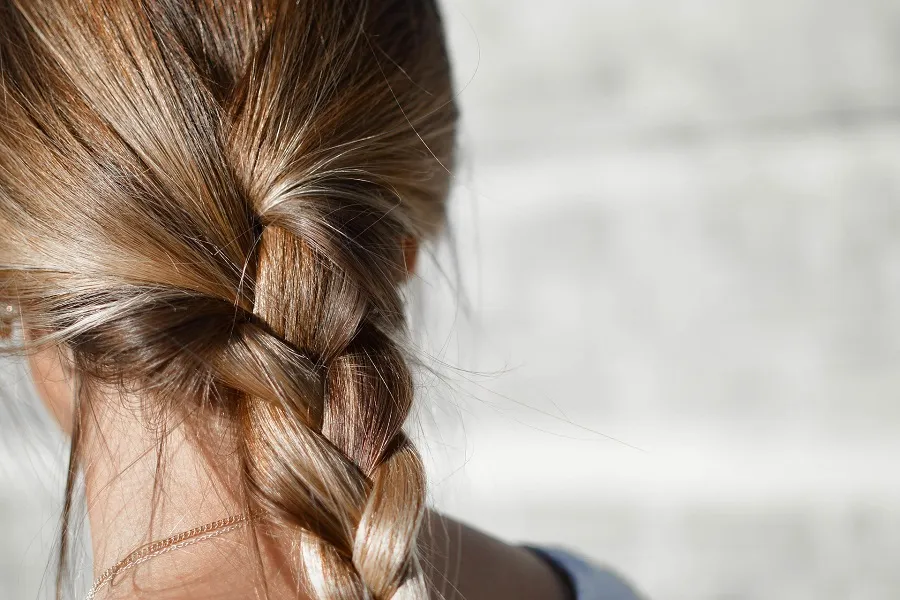 Close-up of a braided hairstyle, showcasing tousled strands in warm blonde tones against a soft, blurred background